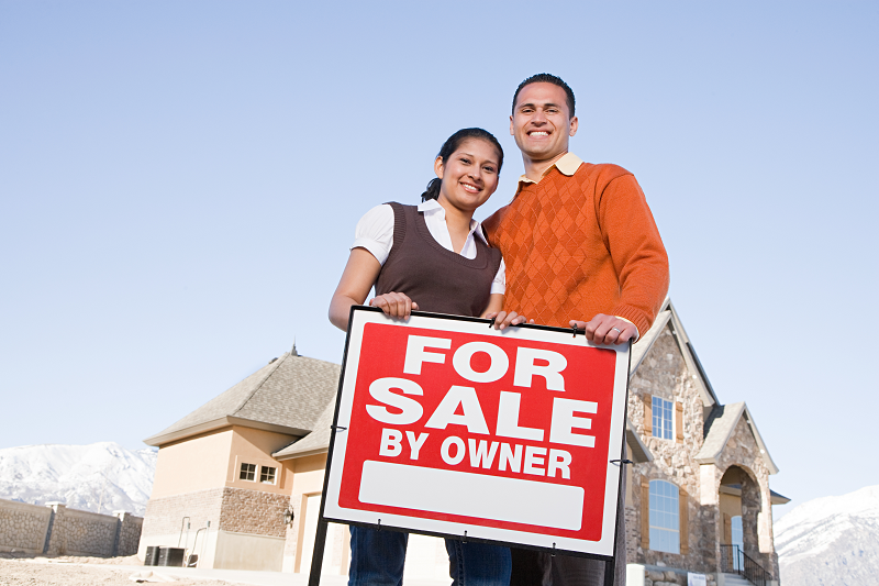 Two house sellers holding a sign that reads "For sale by owner"