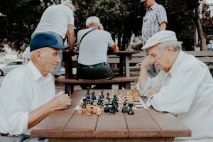 Two older men who have gone through downsizing in Kansas City and are now playing chess outside of a retirement home