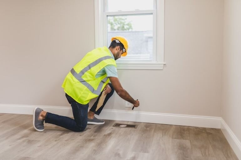 A man with a helmet and a safety vest is checking the floor in a room.