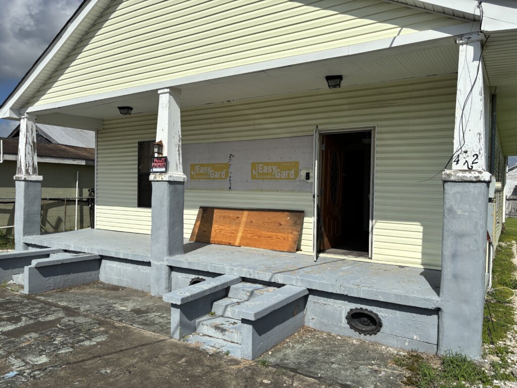 Exterior of an older house with missing vinyl siding and a patchy front lawn, potentially hiding termite damage beneath the surface.