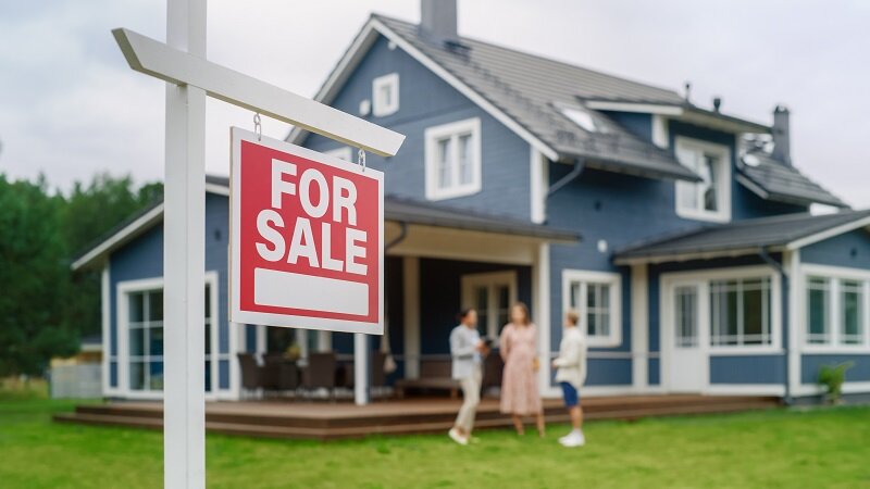 Two young homeowners and their child talk in front of their house after putting their house for sale soon after buying it