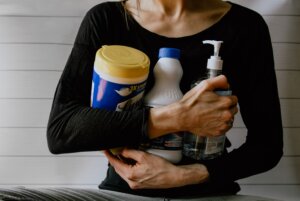 Woman in black shirt holding cleaning supplies.