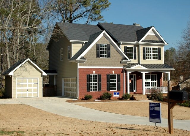 White, gray, and red two-story house with a for sale in North Carolina sign in front of it.