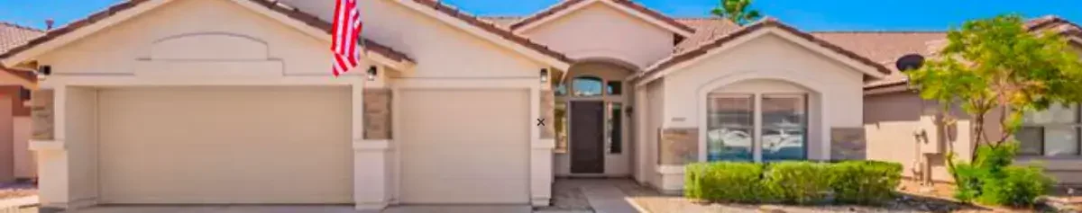 Single-story Phoenix suburban home with a two-car garage, American flag, and desert landscaping.
