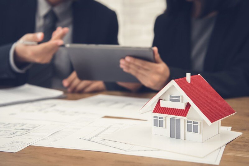 A model house, some documents and files, and a couple of people discussing house prices and the hidden costs of selling a house.