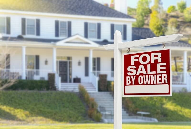 A house with a white and red 'For sale by owner' sign