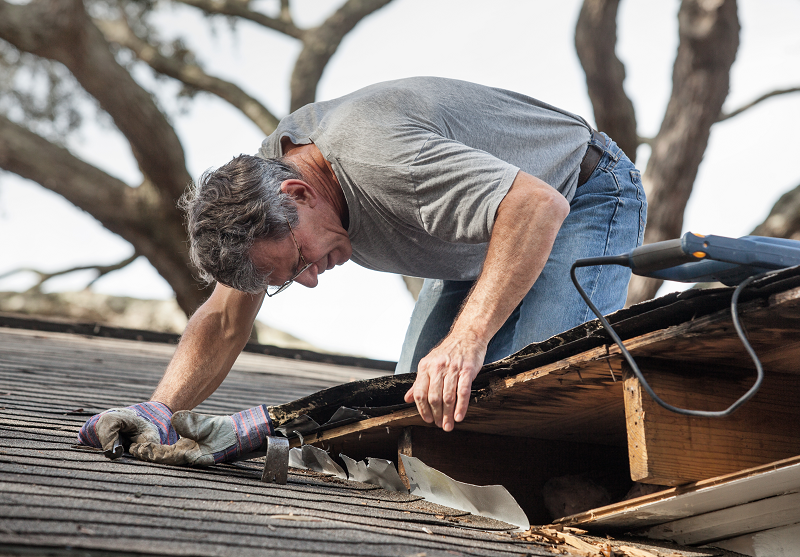 Close-up photo of a homeowner removing rotten wood from his house's roof