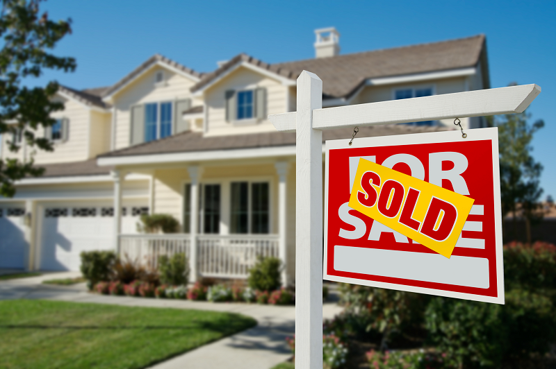 A beautiful white cream house with a white and red "for sale" sign and a yellow "Sold" notice on top of it