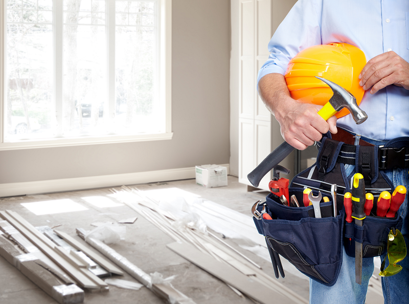 Close up of a homeowner holding a hammer with his hand and a variety of other tools in his tool belt