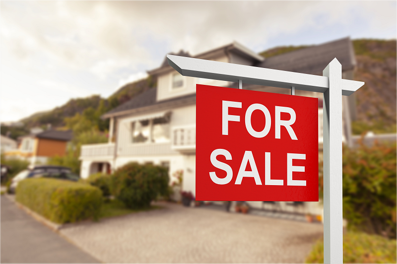 A read "For sale" sign with a beautiful house blurred out in the background