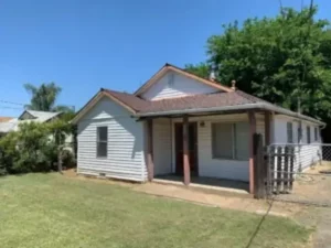 Sell my house fast Sacramento CA image showing a dated white ranch home with a brown roof and simple front yard.