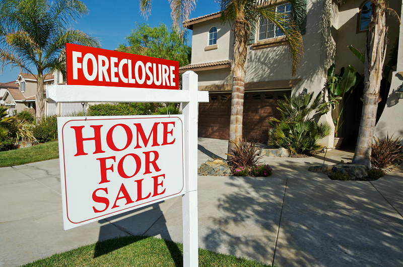 A house for sale with a white and red sign that reads "Foreclosure. Home for sale"