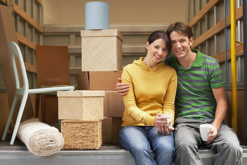 smiling young couple sitting back of moving van