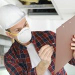 man inspecting a damaged house wearing a dust mask