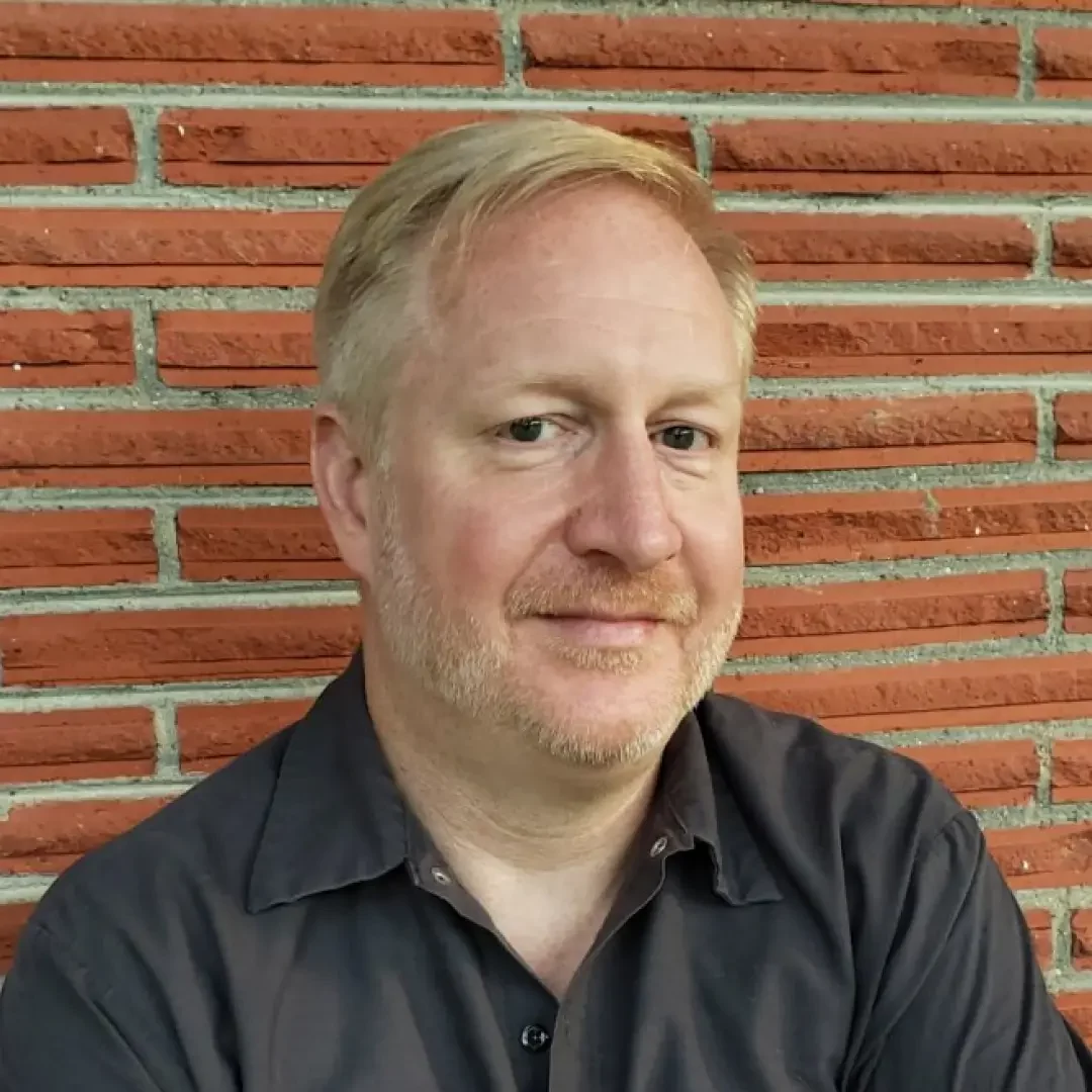 company that buys houses North Richland Hills Cash home buyer near me—portrait of a smiling man standing against a red brick wall, representing local real estate expertise.