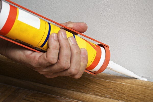 applying caulk between floor and wall