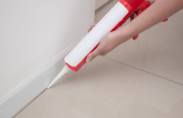 applying caulk between tile floor and baseboard trim