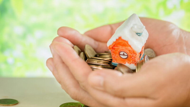 Hand holding a house and some coins