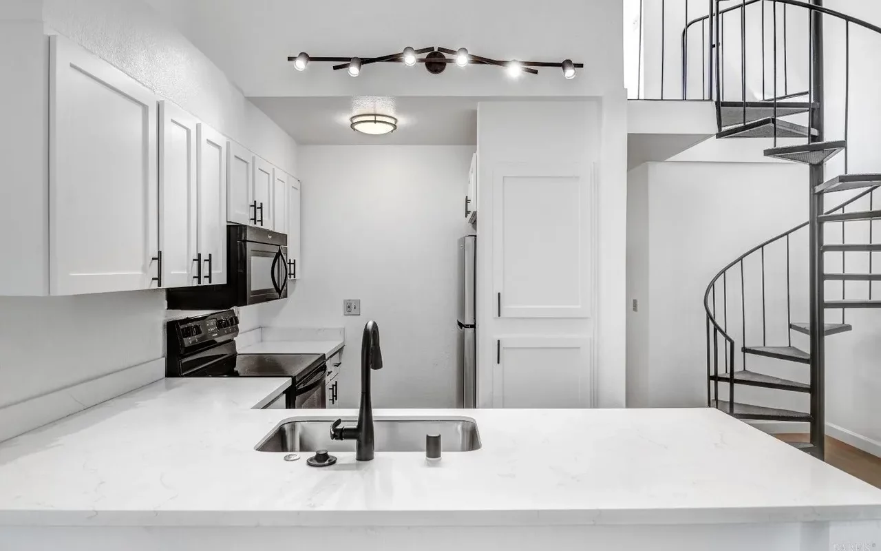 Interior of a Windsor, CA condo kitchen with white cabinets, quartz counters, black fixtures, stainless appliances, and a metal spiral staircase.