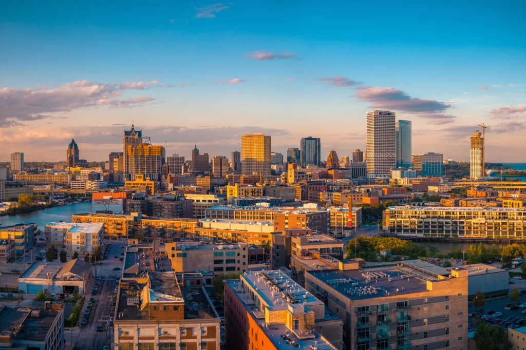 Aerial view of downtown Milwaukee skyline at sunset with modern buildings and Lake Michigan in the background.