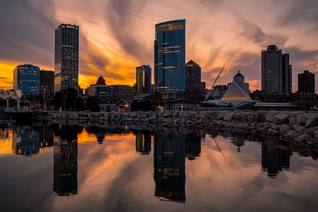 Milwaukee skyline at sunset with tall buildings reflecting on Lake Michigan.
