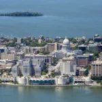 Aerial view of downtown Madison, Wisconsin, featuring the Wisconsin State Capitol surrounded by city buildings and bordered by a large blue lake.