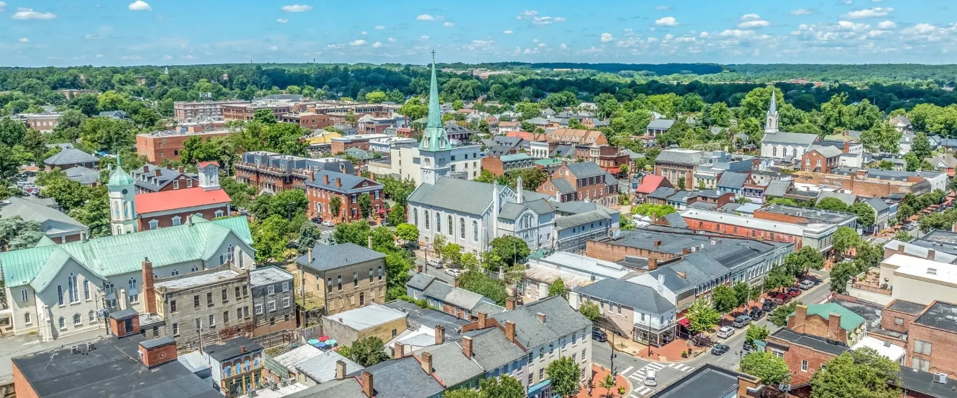 Aerial view of downtown Fredericksburg, Virginia, with historic churches, brick buildings, and tree-lined streets.